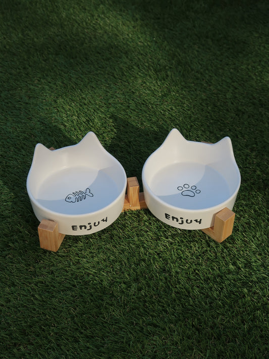 Two white cat-shaped bowls with wooden bases on a green grass background